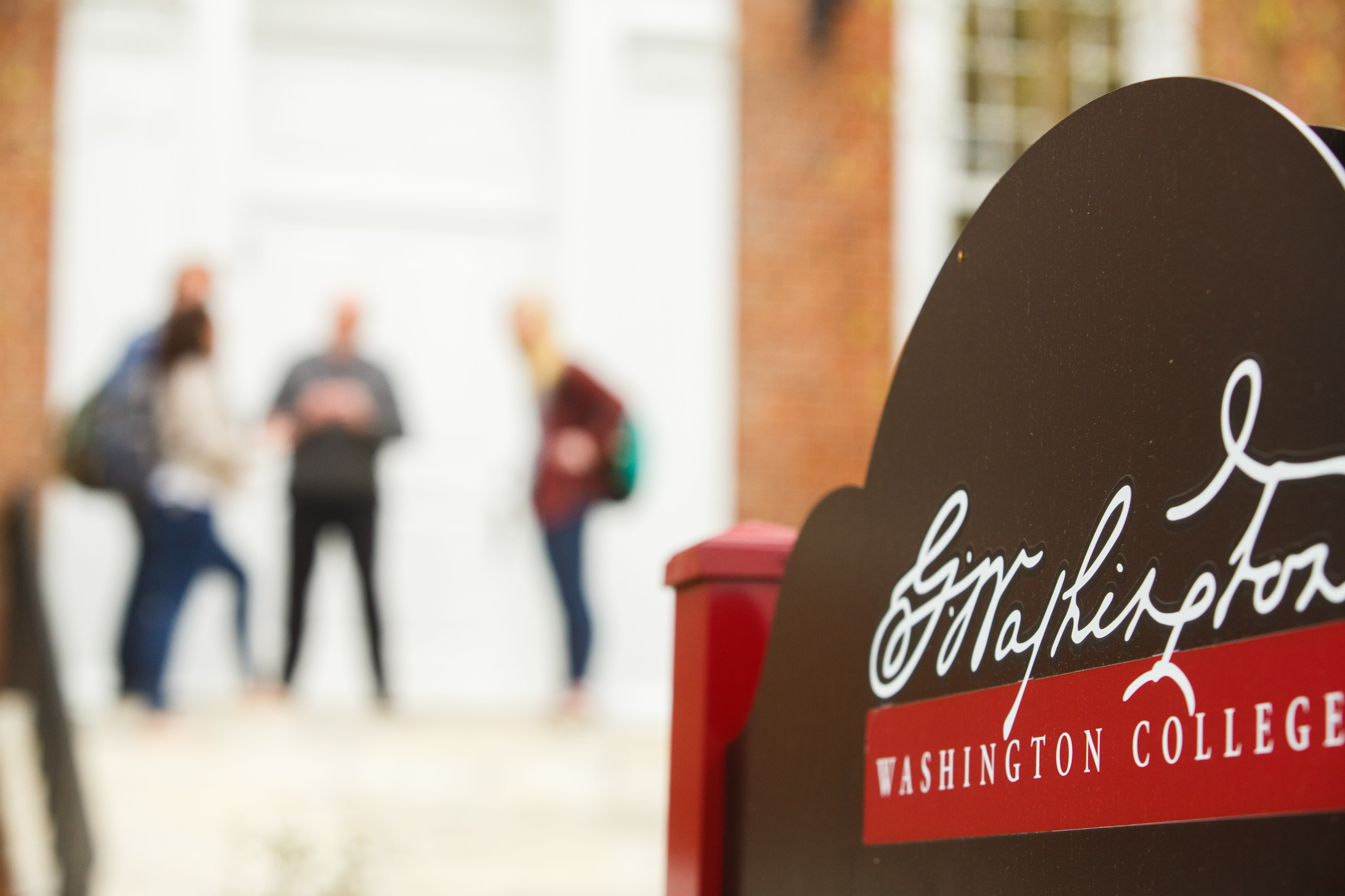 Sign for Washington College. Blurred in background, a group of students stand together.