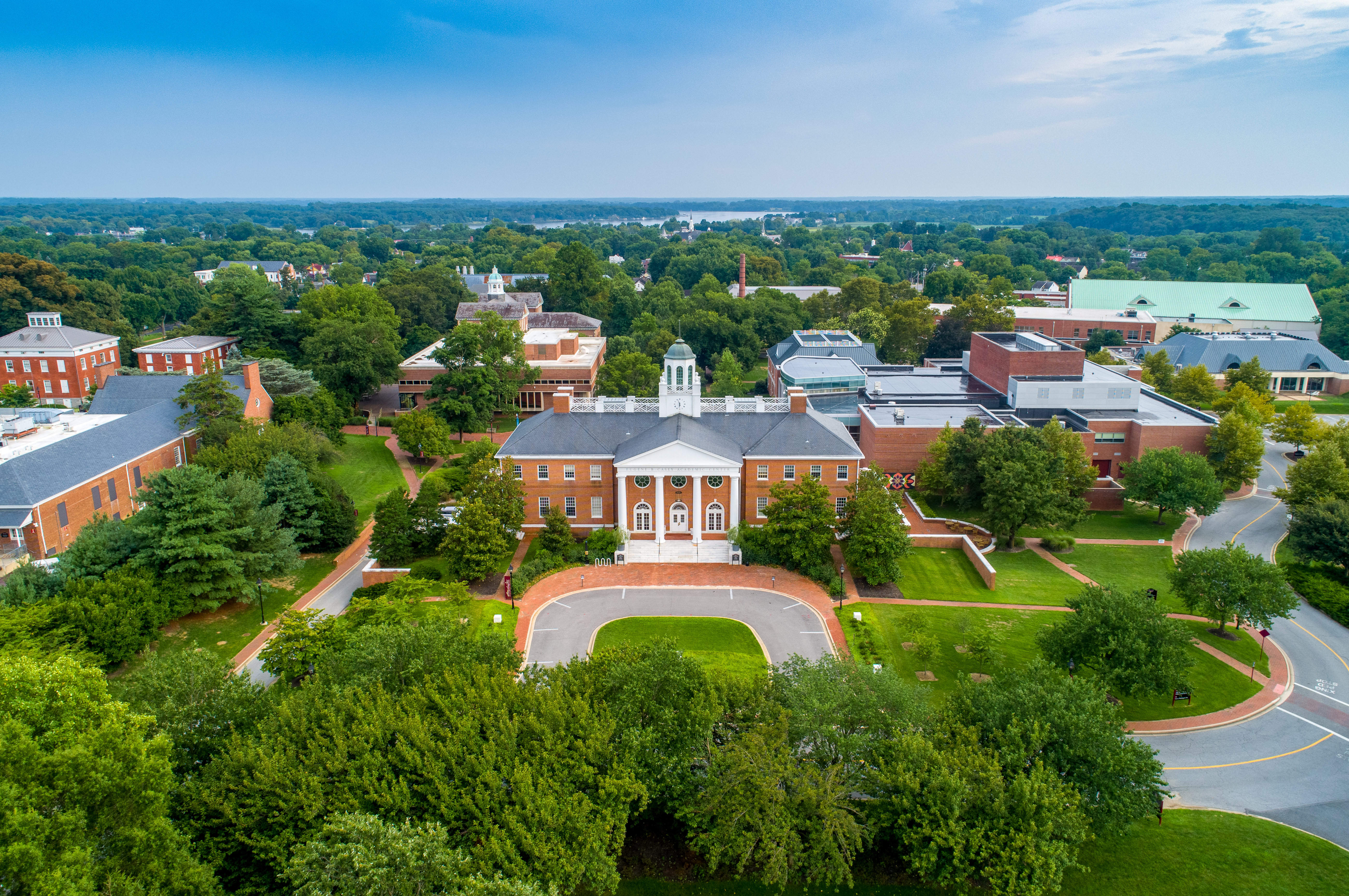 birds eye view of the casey academic center and campus during the spring. the sky is clear and the trees are lushious green