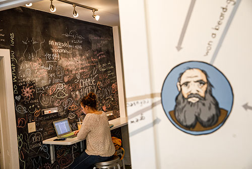 Student sitting at counter in Literary House kitchenette in front of chalkboard wall with phrases and words written in chalk