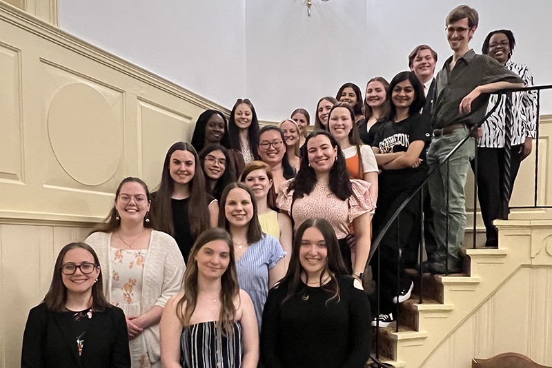 The 2023 Class of Washington College's Chapter of Phi Beta Kappa smile for a portrait from the staircase in Hynson Lounge