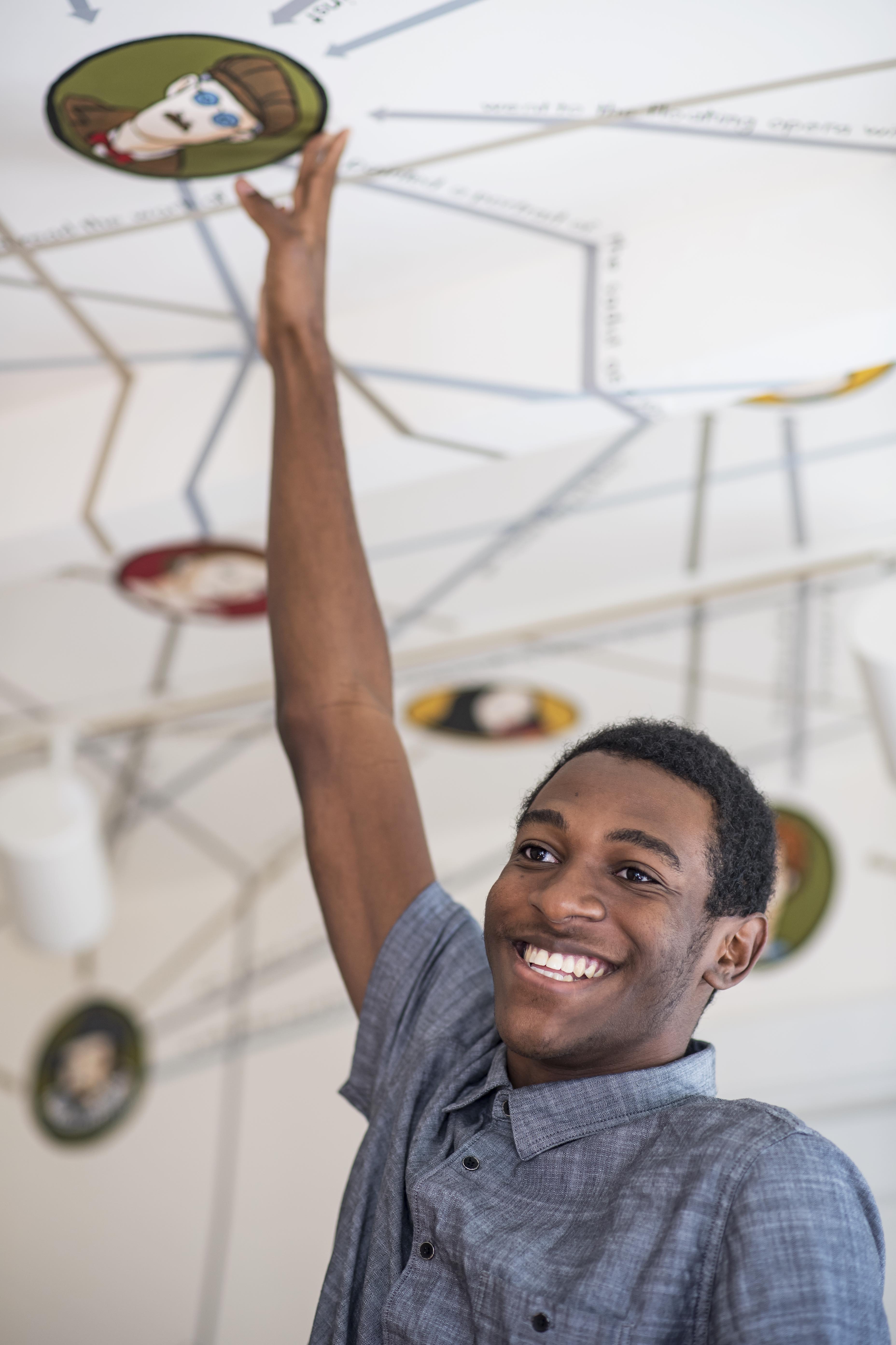 Dante, wearing a blue shirt, smiling as he reaches towards the ceiling of the Rose O'Neill Literary House.